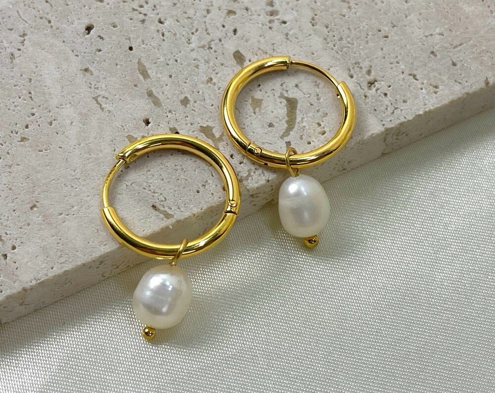 Close-up of textured, gold-colored hoop earrings with a pearl drop attached to each hoop.