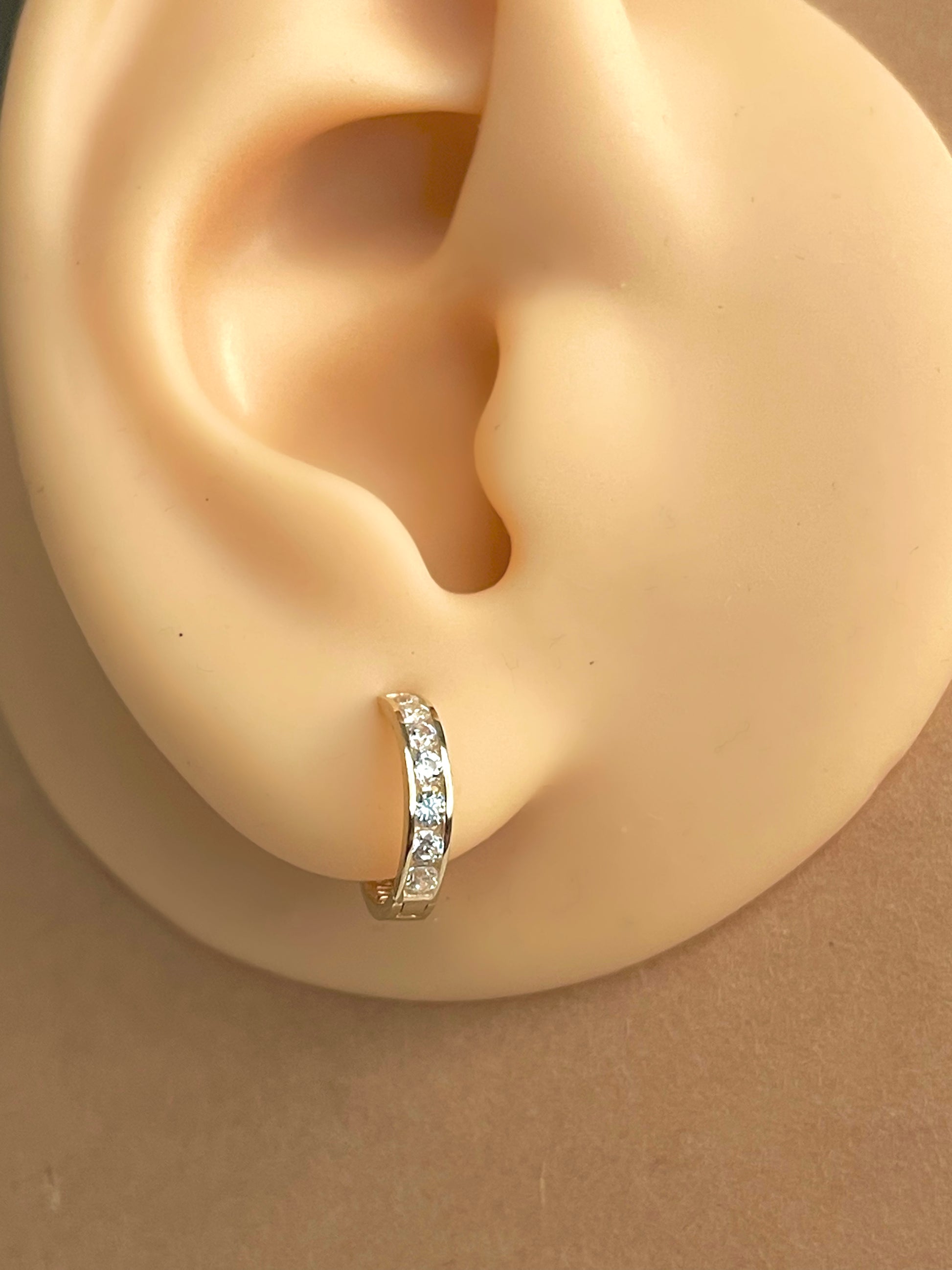 A single gold hoop earring with a row of small, clear gemstones set around the circumference. The earring is worn in a person's ear.