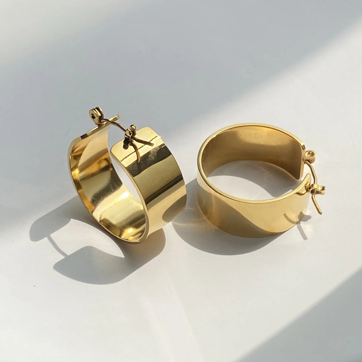 Pair of Gold Basic Hoop Earrings. They are round-shaped with a wide, flat design and are gold-plated.