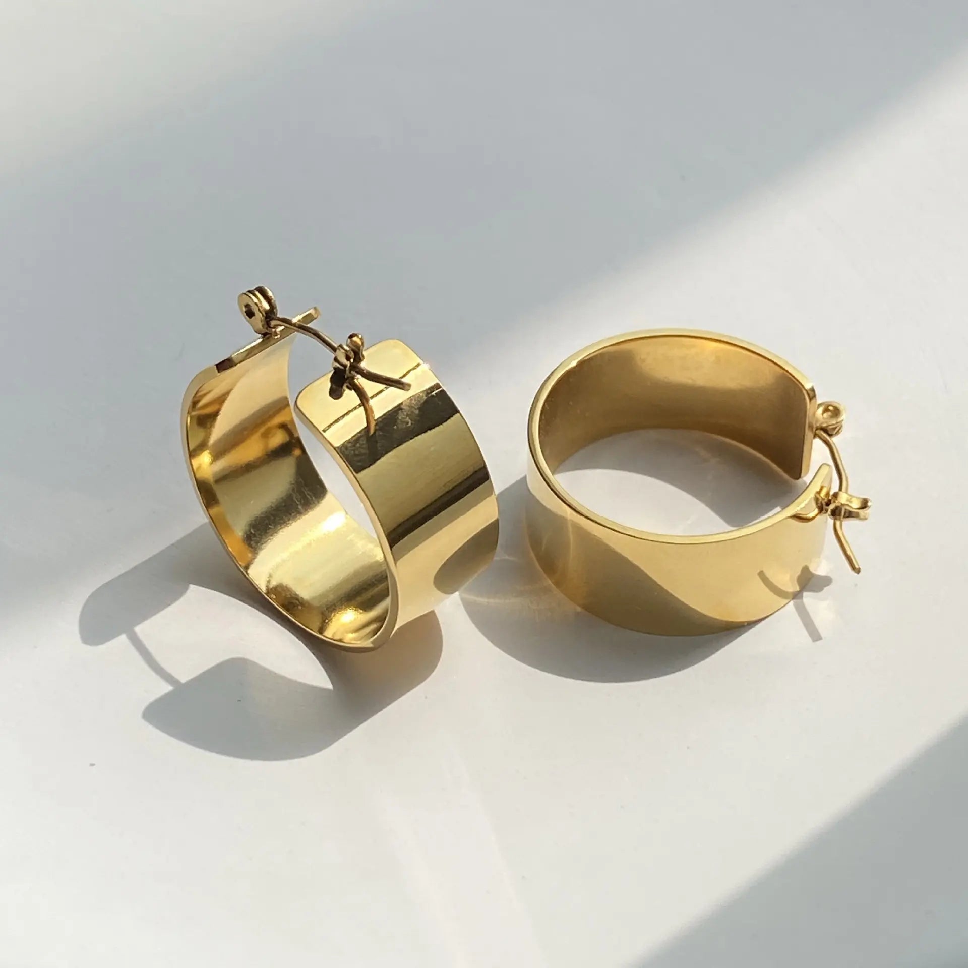 Pair of Gold Basic Hoop Earrings. They are round-shaped with a wide, flat design and are gold-plated.