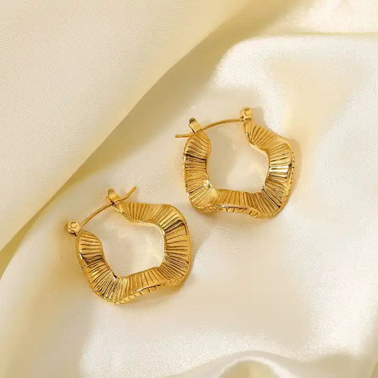 Close-up of textured, gold-colored hoop earrings with a wavy or pleated pattern.