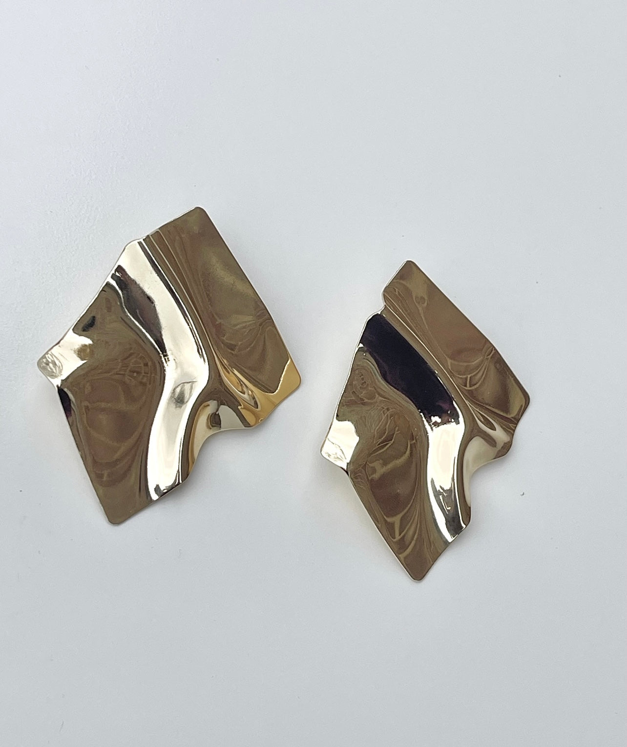 A pair of large, gold square earrings with a textured, crumpled surface. The earrings are resting on a white background.