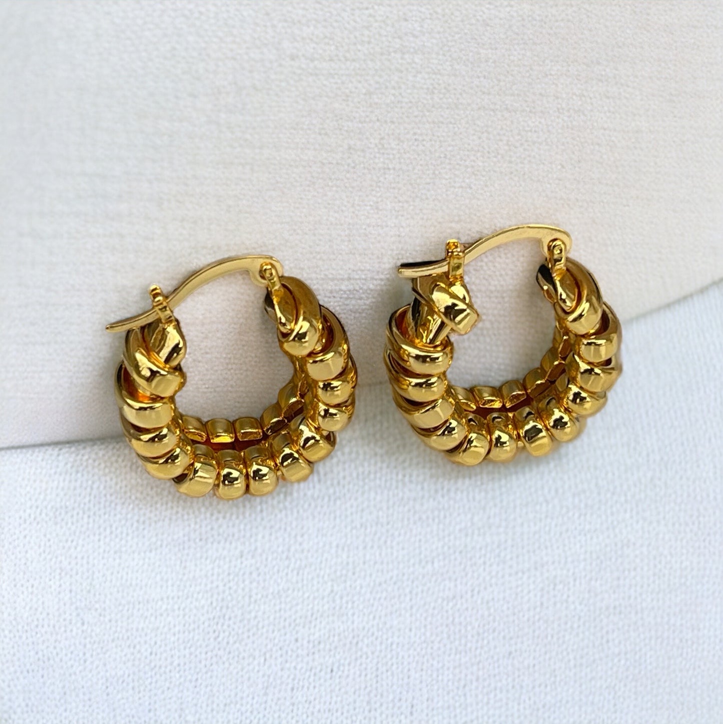 Close-up of textured, gold-colored hoop earrings with a coiled or ribbed pattern.