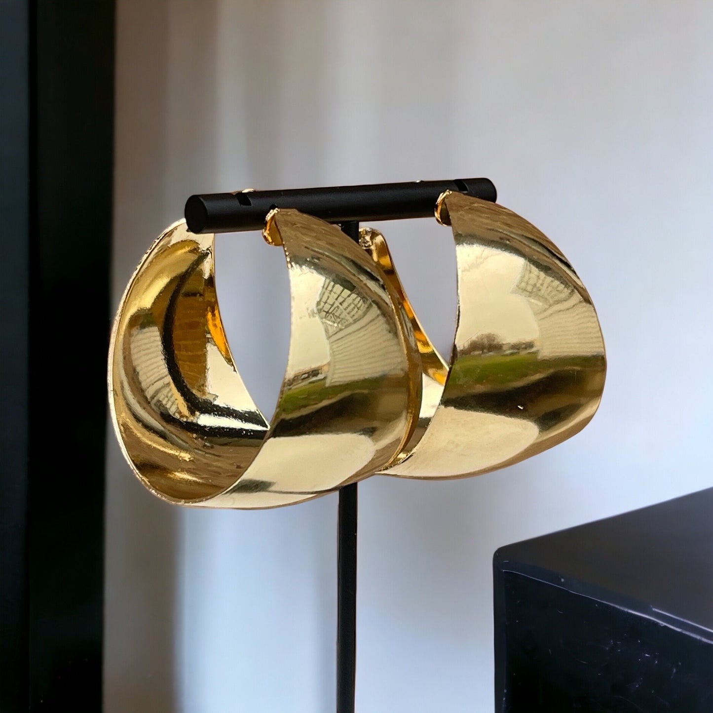 Pair of oversized statement hoop earrings in gold. They are large, thick, and have a curved, almost teardrop shape. The earrings appear to be made of a smooth, shiny metal.