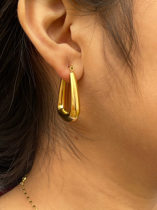 A pair of large, gold-colored hoop earrings with a slightly elongated, teardrop shape.