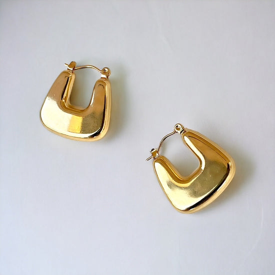 The image shows a pair of gold U-shaped square earrings. They are chunky and have a bold, geometric design. The earrings appear to be made of a smooth, shiny metal.