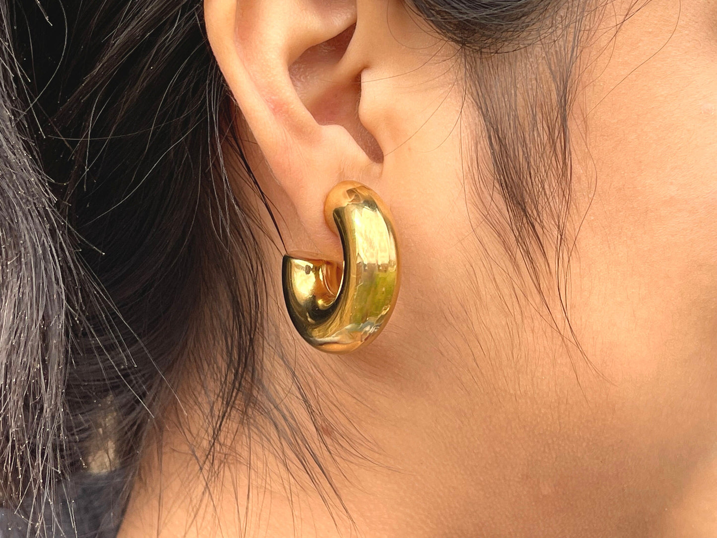 A large, gold hoop earring with a thick, rounded design. The earring is worn in a woman's ear.