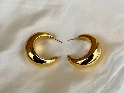 Oversized, gold-toned hoop earrings with a smooth, curved surface. 