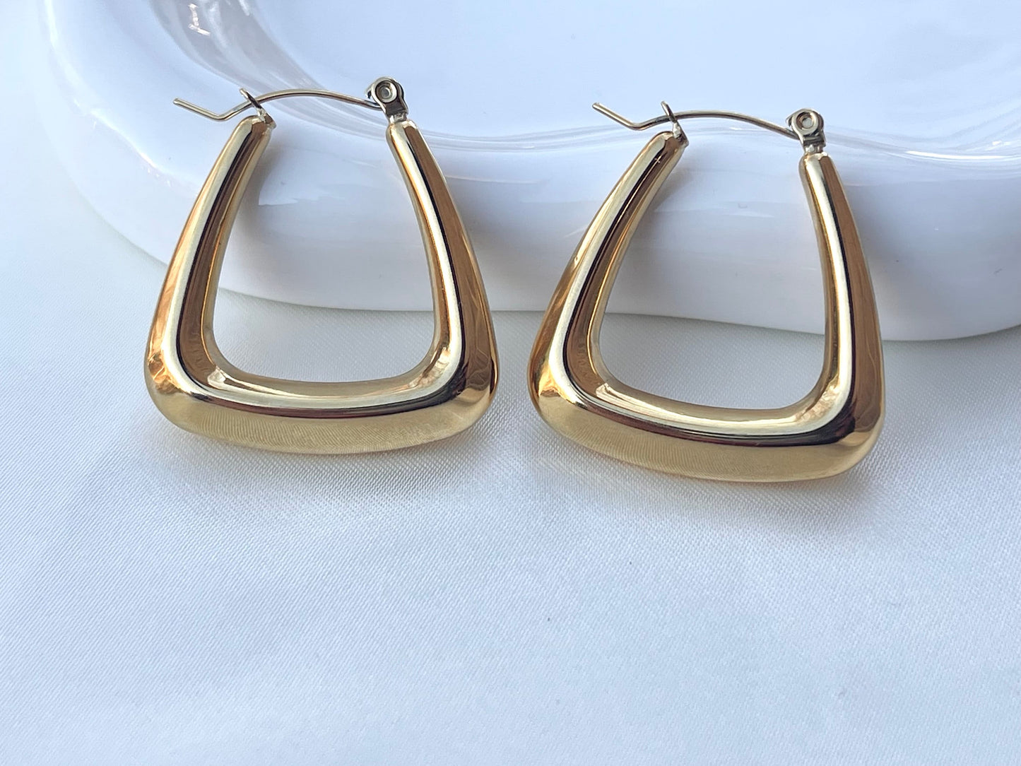 A pair of large, gold-colored hoop earrings with a geometric, triangular shape.