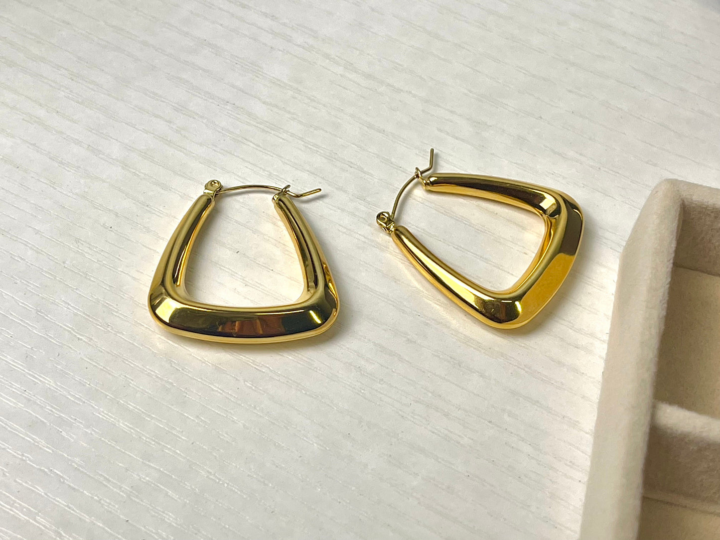 A pair of large, gold-colored hoop earrings with a geometric, triangular shape.