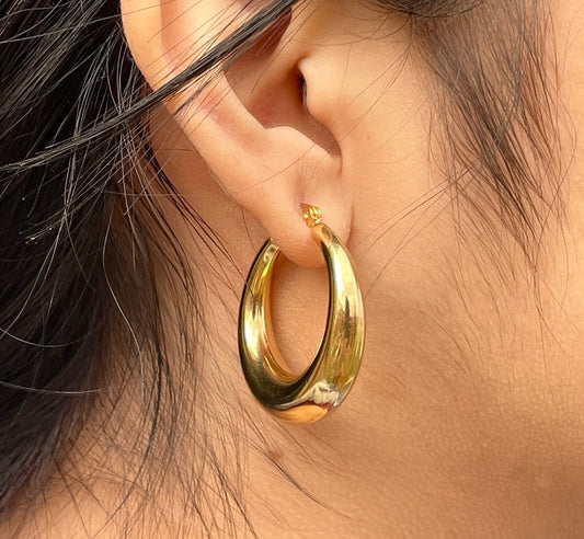 Pair of elegant gold medium hoop earrings. The earrings have a distinctive oval shape and a slightly puffed design.