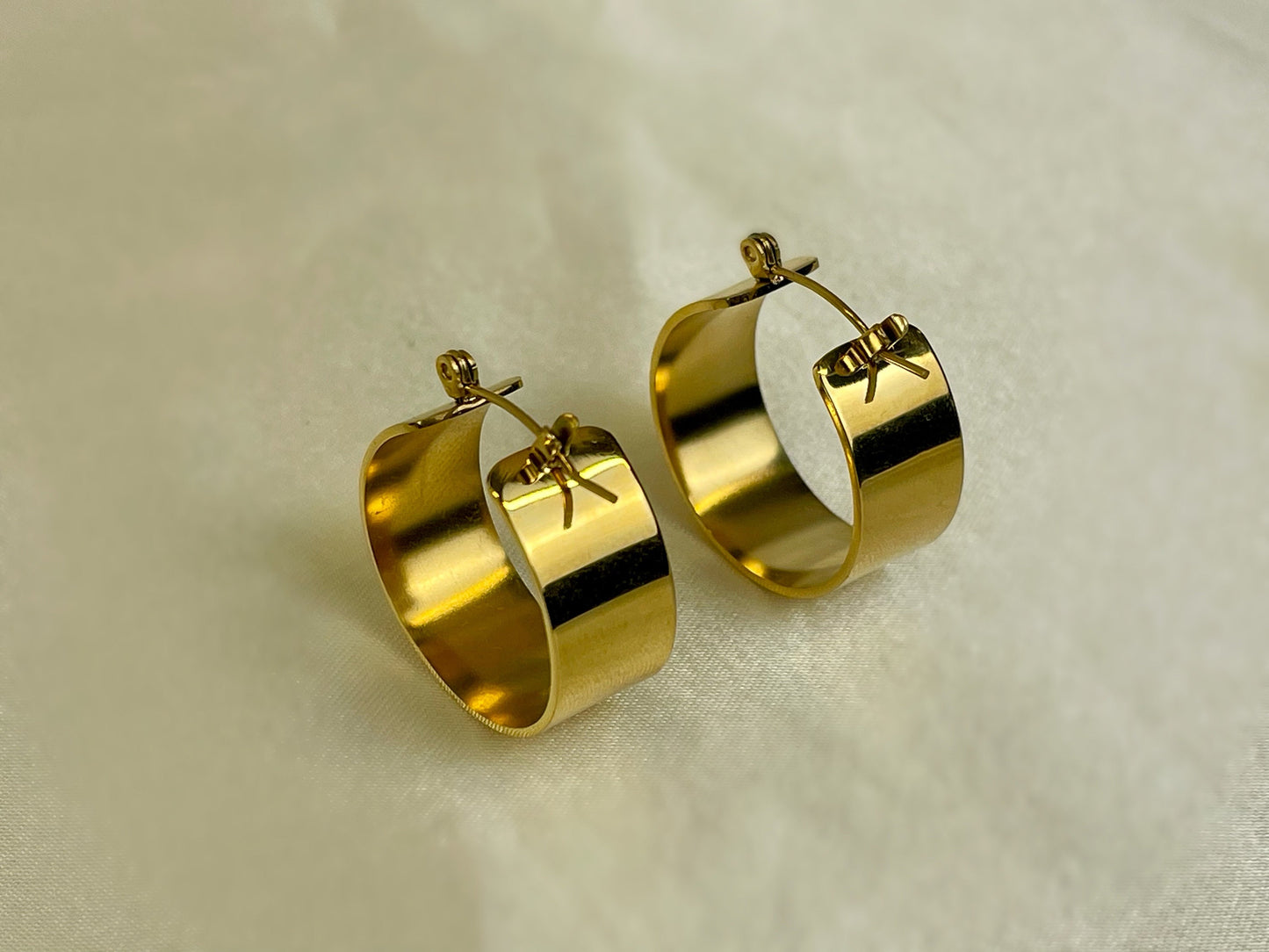 Close-up of textured, gold-colored hoop earrings with a flat, wide design.