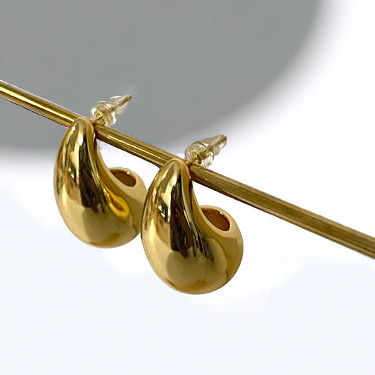 A pair of large, gold hoop earrings with a teardrop shape. The earrings are hanging from a metal bar.